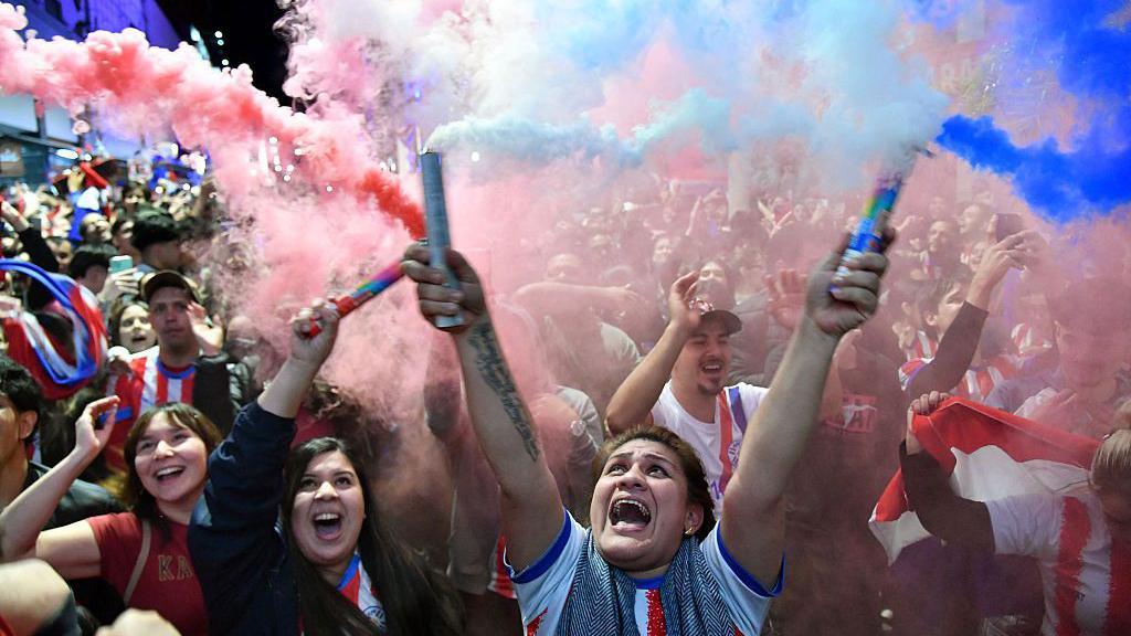 A woman holiding up two flares in the street as the citizens of Asunscion party hard following Paraguay's victory against Germany