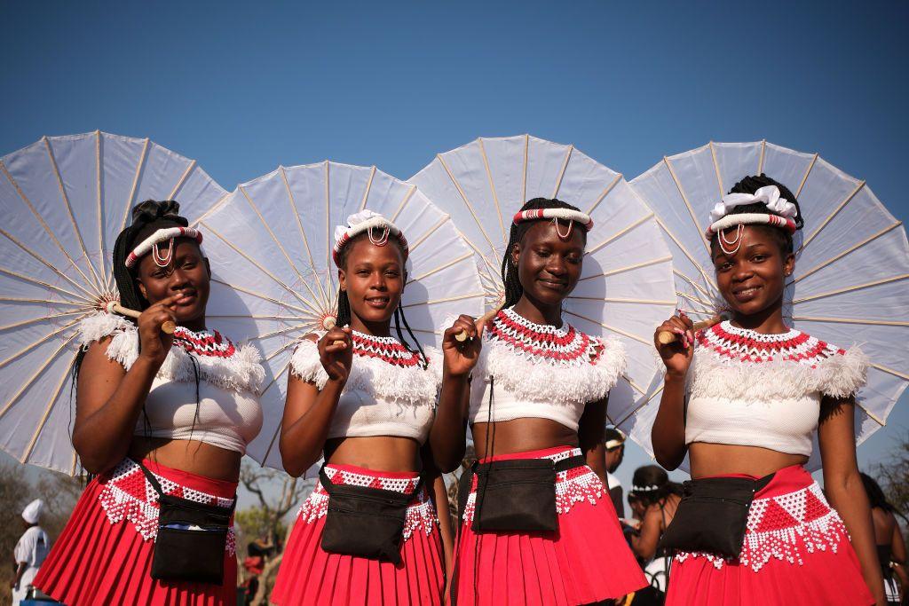 Young women wear matching red-and-white outfits and carry matching parasols.