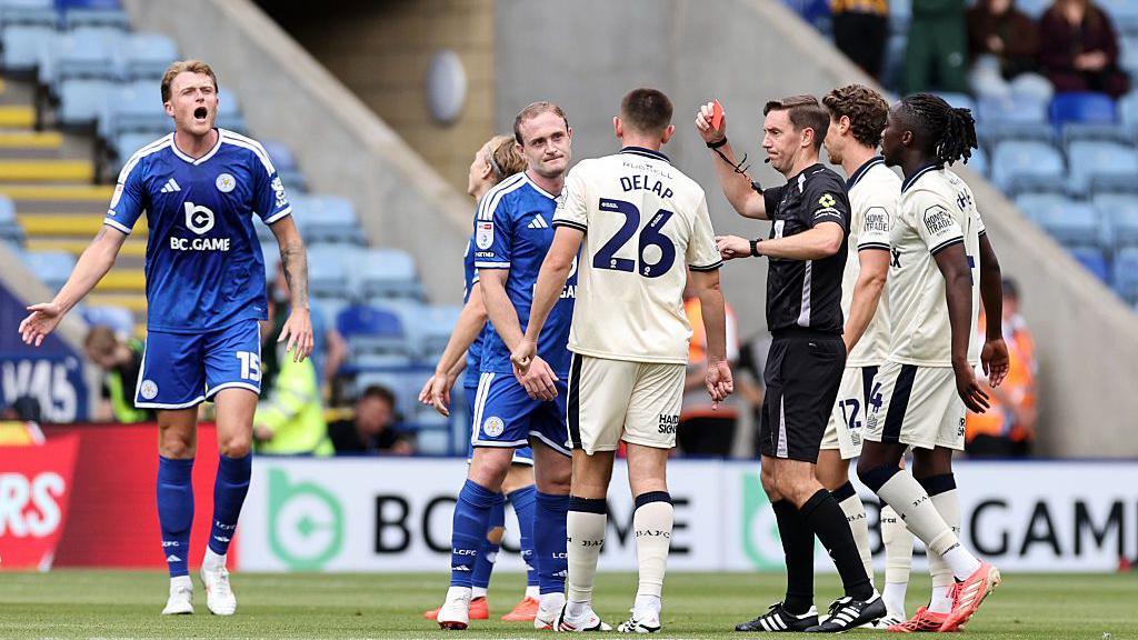 Referee Ben Toner shows a red card to Oliver Skipp of Leicester City
