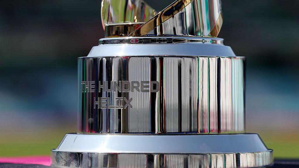 A close-up of The Hundred Helix trophy, which shows the text 'The Hundred Helix' inscribed on the side.