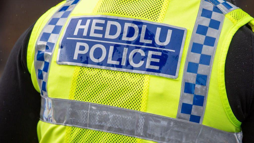 The back of a hi-vis police with the words Heddlu Police in silver with a blue back background