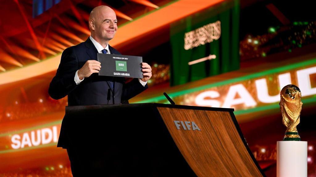 Gianni Infantino holds up a card and stands next to the World Cup trophy