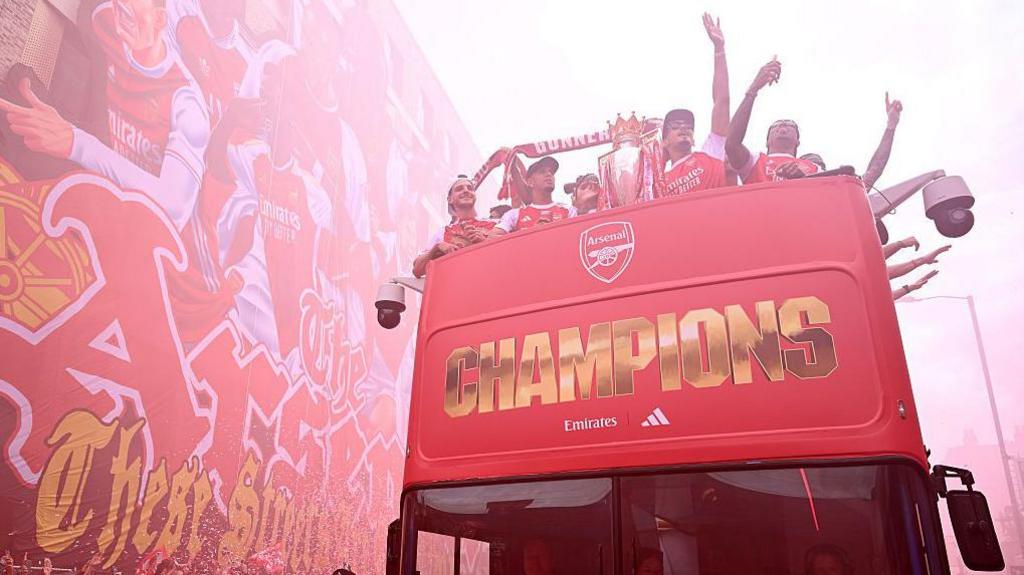 Arsenal players celebrate as the bus moves next to the Tifo