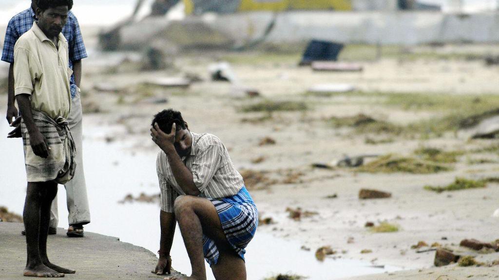 Indian men stand exhausetd after searching for missing relatives at Silver Beach in Cuddalore, some 185 kms south of Madras, 27 December 2004, after tidal waves hit the region. 