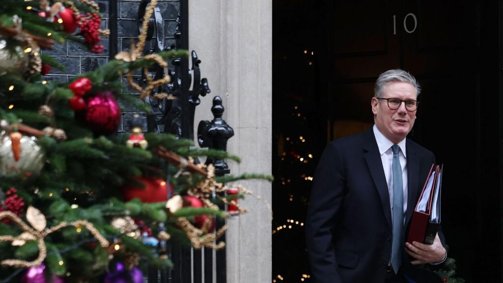 Starmer leaves No 10 with folders under his arm. On the left is a Christmas tree in Downing Street
