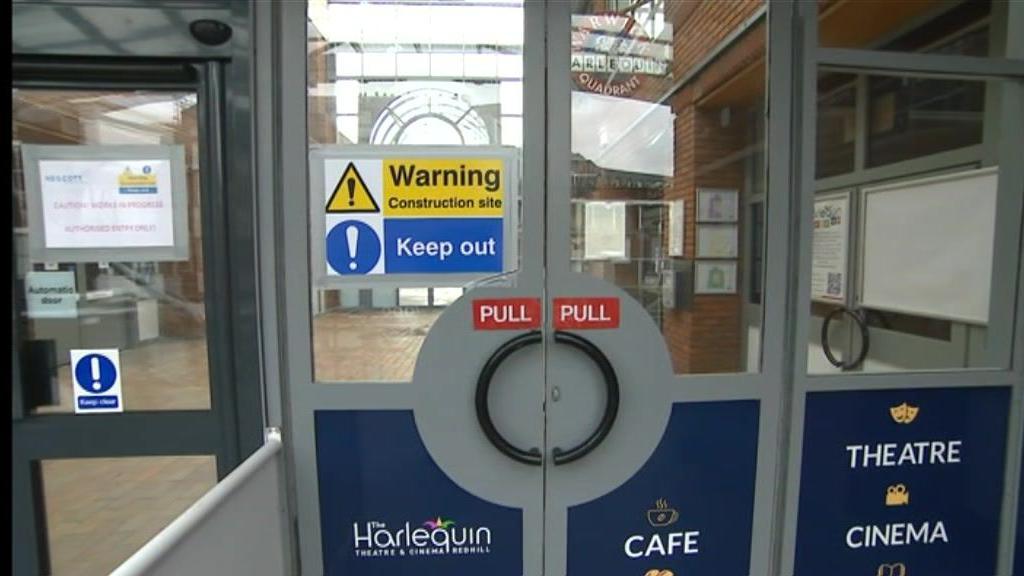 The main entrance to the Harlequin Theatre in Redhill, showing a sign telling people to keep out due to it being a construction site.