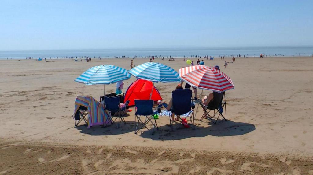 Group of people sit on deckchairs on the beach with striped parasols above them