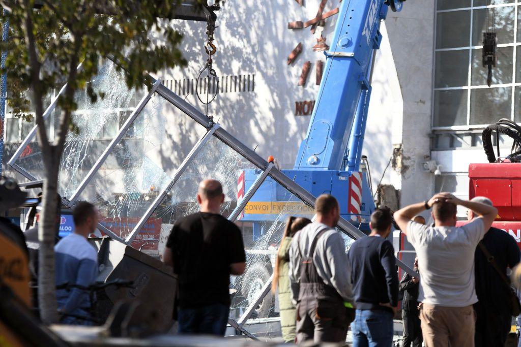 Men stand in front of a crane and a smashed glass structure outside a railway station in Serbia