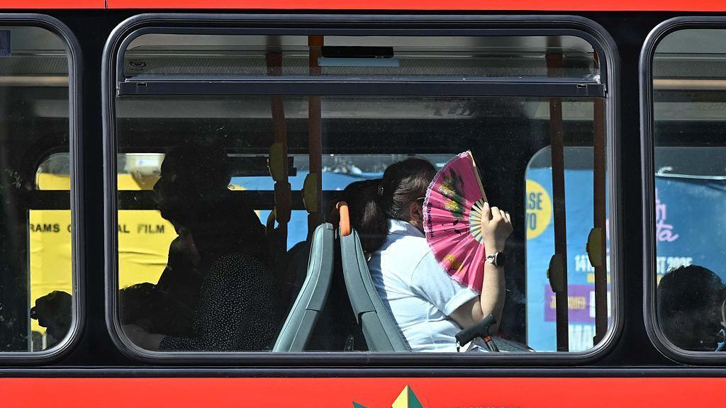 A woman holding a fan on a bus.