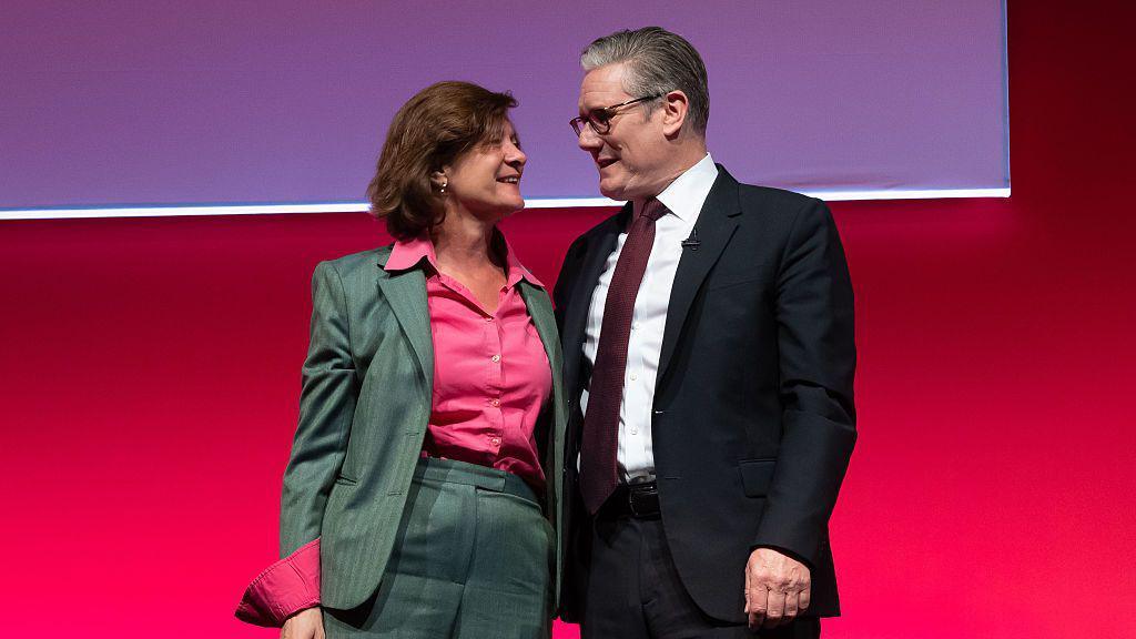 Eluned Morgan, in a grey suit and wearing a pink shirt, embraces Sir Keir Starmer, wearing a dark suit, white shirt, glasses and a dark red tie