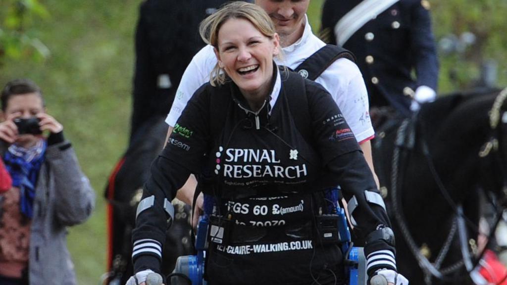 Claire Lomas completing the London Marathon in 2012. She wears a black top with "Spinal Research" written on it and has blue machinery supporting her hips and holds two crutches