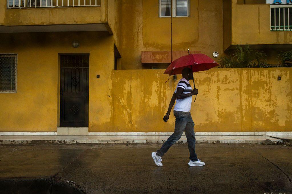 A man with an umbrella walks down a street during Senegal's rainy season.