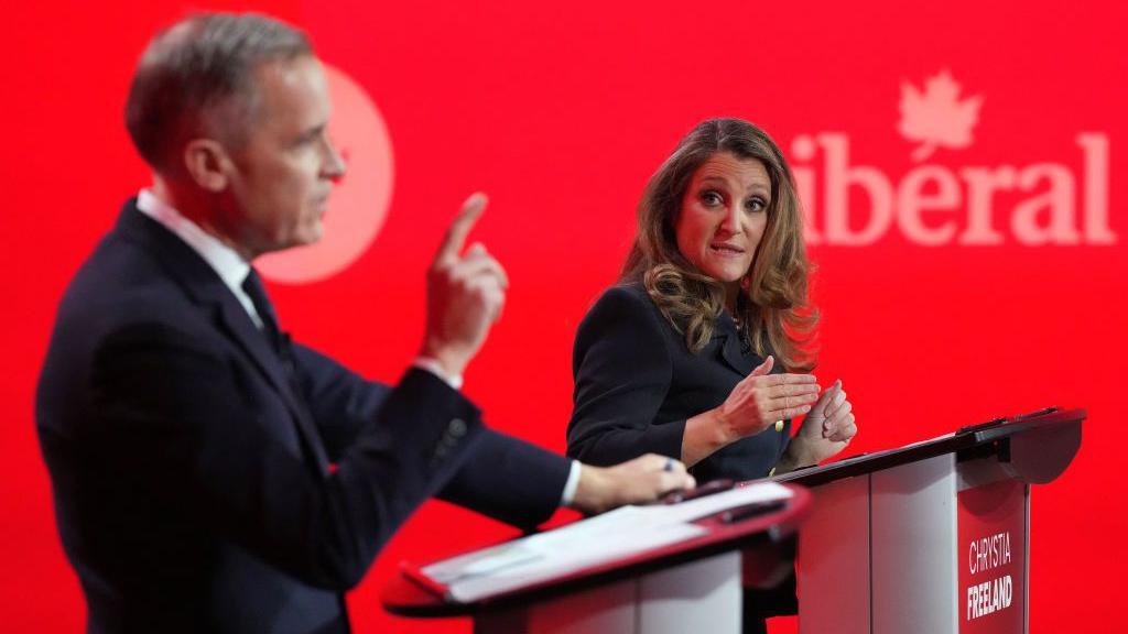 Chrystia Freeland and Mark Carney speaking at their respective podiums during the debate