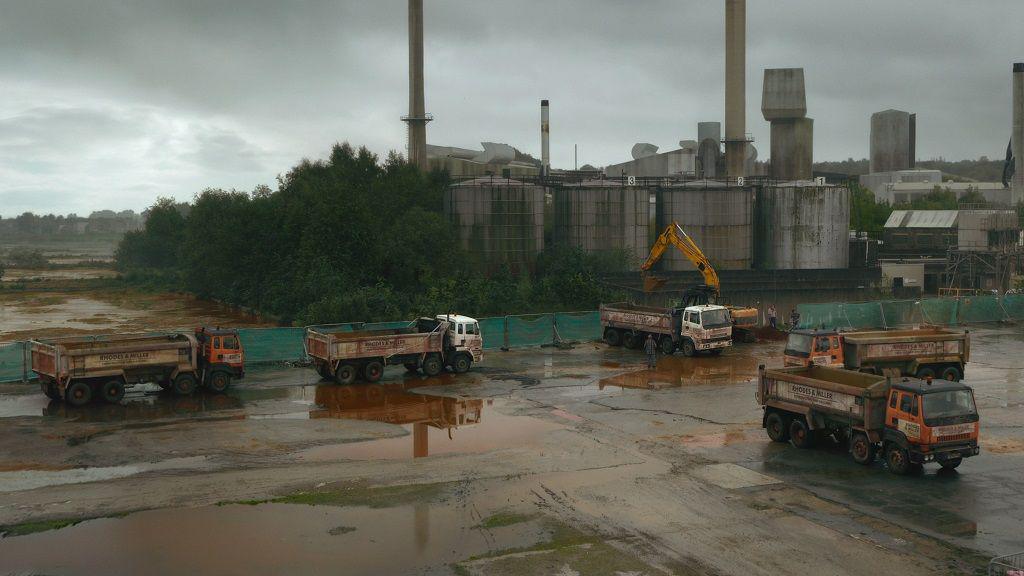 Five truck are parked in the muddy area outside an abandoned factory site in a still from Toxic Town.