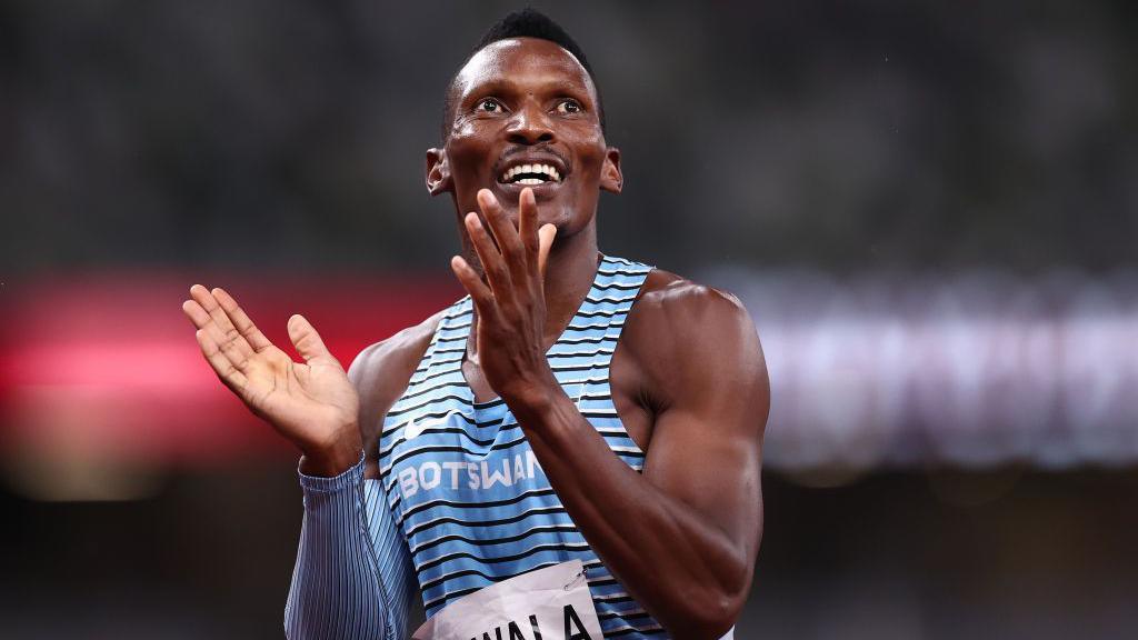 Isaac Makwala shown from stomach up wearing a blue and black striped Botswana sleeveless running jersey reacts as he is seen midway through clapping his hands during the men's 400m event at the Tokyo 2020 Olympic Games 