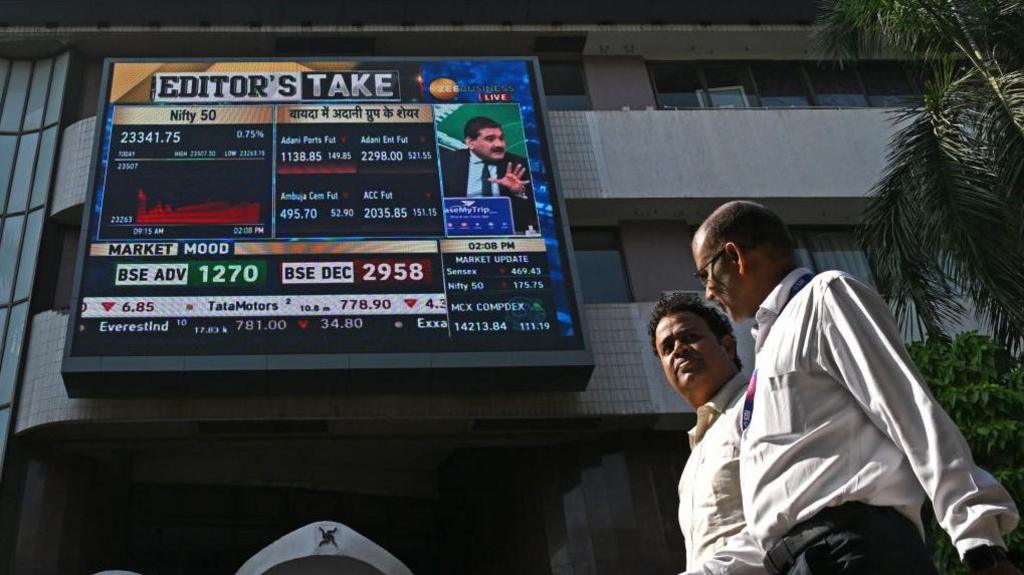 Pedestrians walk past a digital broadcast on the facade of Bombay Stock Exchange (BSE) in Mumbai on November 21, 2024. Shares in Indian conglomerate Adani tanked on November 21 after its industrialist owner Gautam Adani was charged by US prosecutors with handing out more than $250 million in bribes for key contracts.