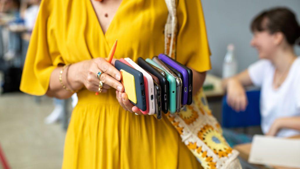 Women in yellow dress holds multiple cell phones in her hands