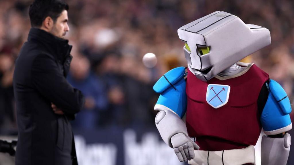 Mikel Arteta, Manager of Arsenal, looks on as Hammerhead, Mascot of West Ham United, walks past prior to during the Premier League match between West Ham United FC and Arsenal FC at London Stadium