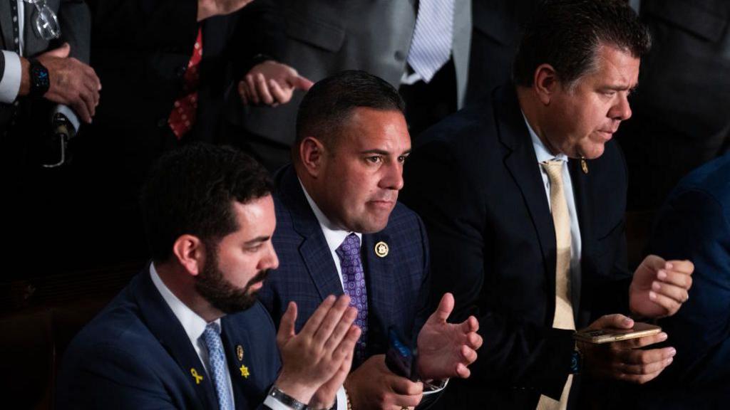 Mike Lawler, Anthony D'Esposito and Nick LaLota, all wearing suits and ties, stand and applaud during a congressional session