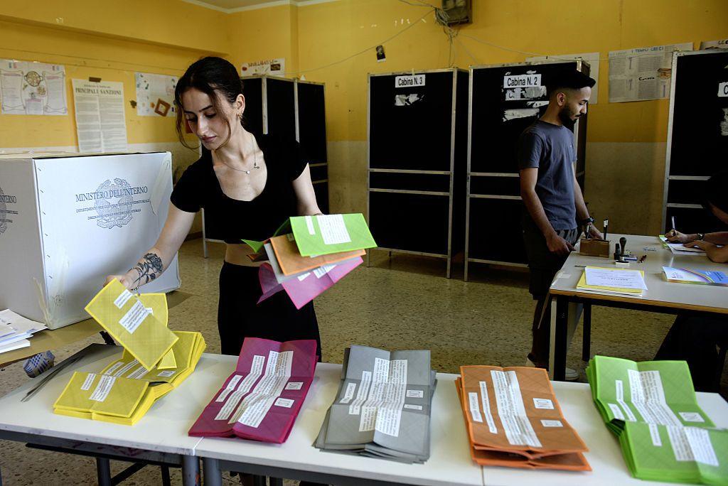 A woman wearing all black lays out multi-coloured referendum cards in a polling station in Italy.