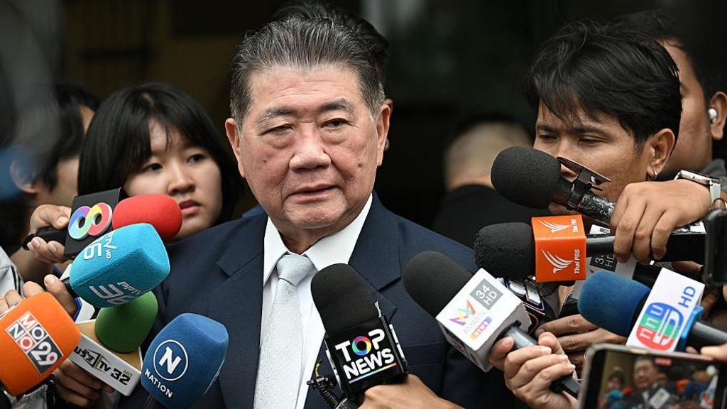 Thailand's acting Prime minister Phumtham Wechayachai surroundeed by mics as reporters as ask him questions. He is wearing a balck suit.