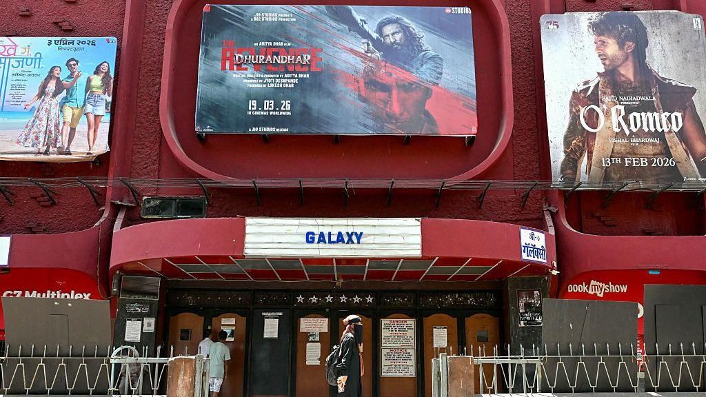 A woman walks past a poster of Indian Hindi-language spy action thriller film Dhurandhar: The Revenge (C), displayed outside a cinema hall in Mumbai on April 7, 2026.