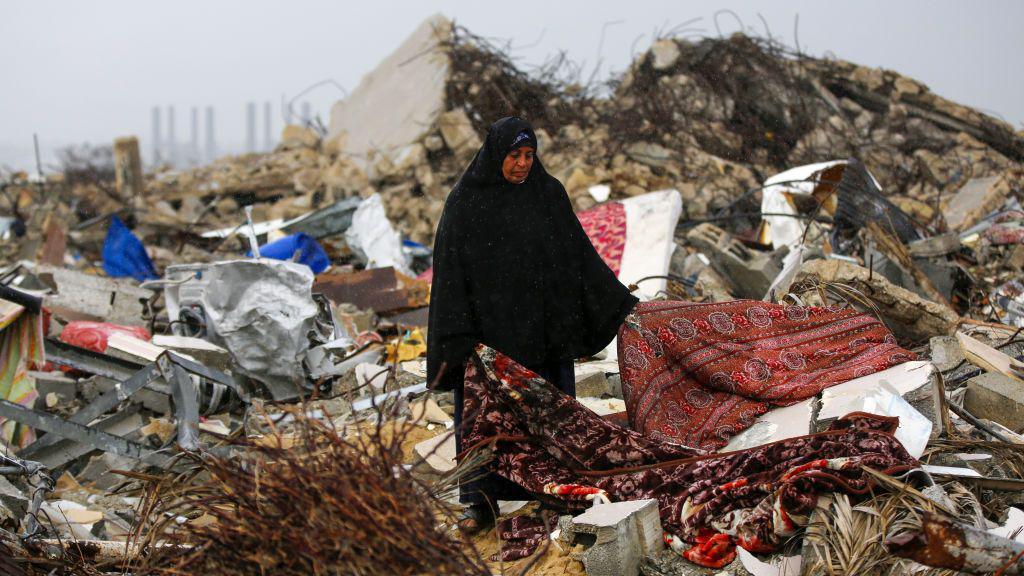 A displaced Palestinian woman searchers for rugs to use in a tent set up among the rubble of destroyed buildings in the al-Mughraqa area of central Gaza (12 February 2025)