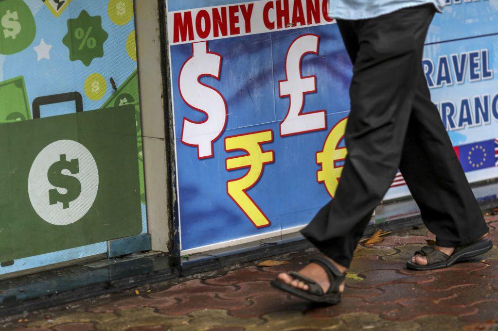 A wall with a money change board and a man walking past. Only his legs are seen.