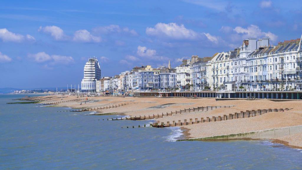 A line of pretty white houses along a beach. The sky is blue with small clouds. 