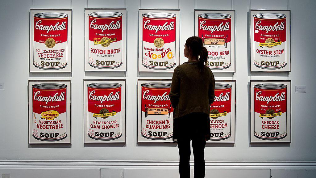 Gallery assistant stands in front of Andy Warhol's iconic Campbell's Soup Can paintings.