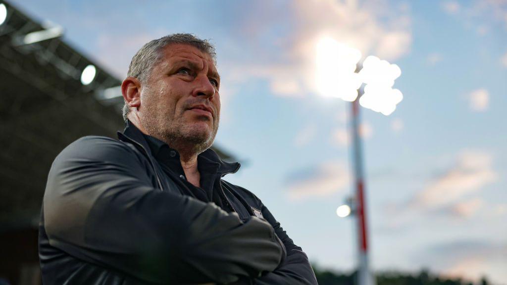 Osian Roberts with arms folded looks out over a floodlit pitch