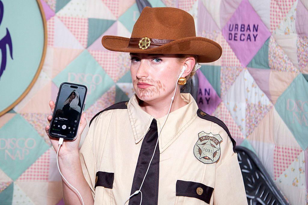 Amelia Dimoldenberg shows how she's listening to a Lily Allen song while dressed as a sheriff