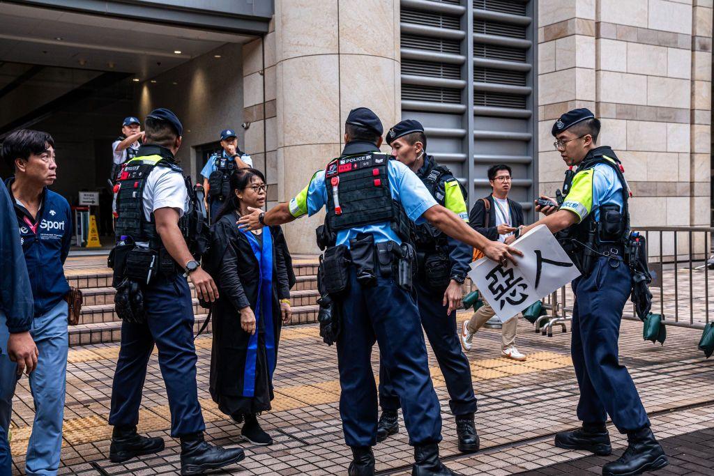 Police officers remove a protest banner from Elsa Wu, the foster mother of one of the defendants Hendrick Lui, as she leaves the West Kowloon Court following a sentencing hearing for 45 pro-democracy activists in Hong Kong, China, on Tuesday, Nov. 19, 2024.