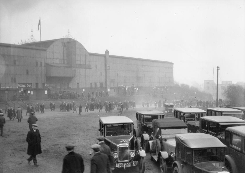 Cars parked outside and pedestrians approaching St James Park in 1930