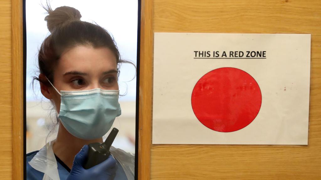 File photo dated from January 2021 of a nurse communicating via a walkie-talkie behind a door with a sign on it with a bit red dot and the words 'this is a red zone'