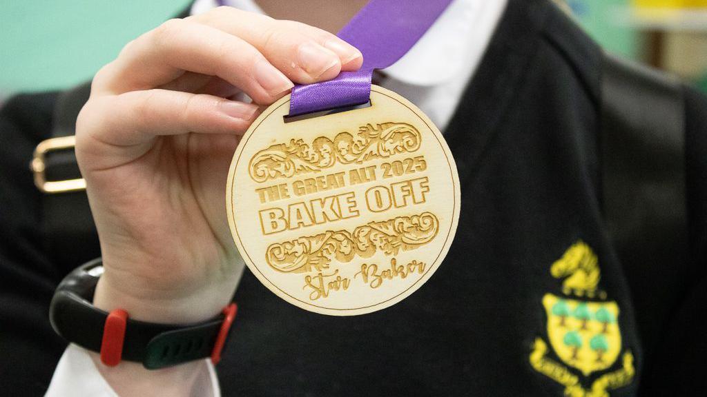 Close-up of a teenagers hand holding a gold medal saying 'The Great ALT 2025 Bake Off, Star Baker'