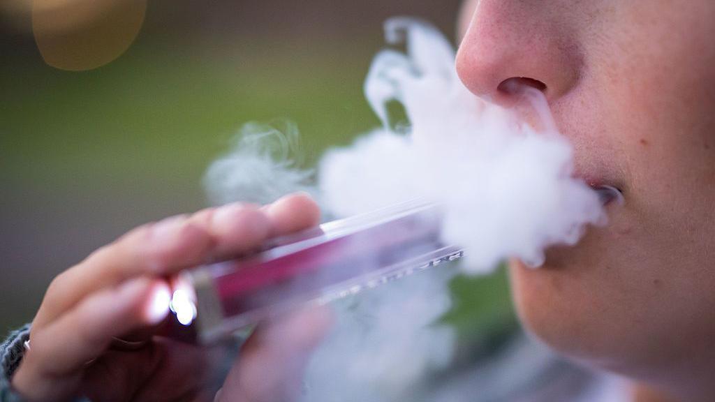 A person holds a vape up to their mouth