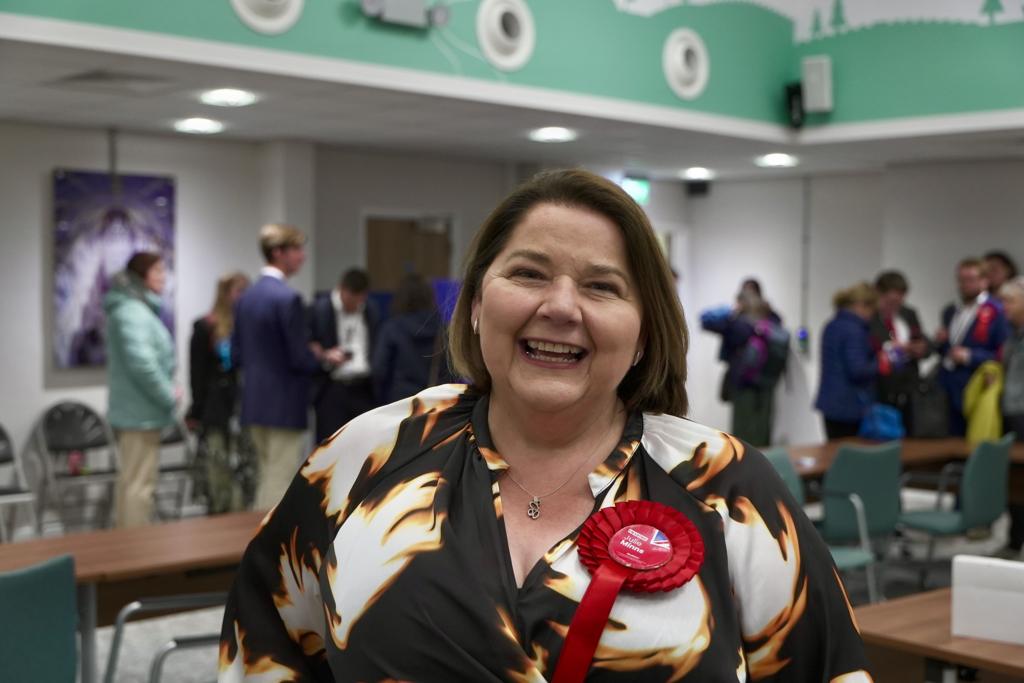 Labour's Julie Minns wearing a patterned dress and a red rosette celebrates winning in Carlisle