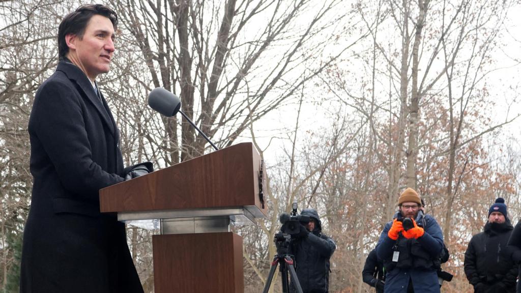 A side profile view of Justin Trudeau standing at a podium wearing a winter coat