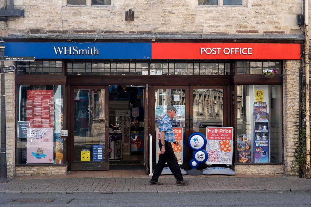 Man walks past a shop with blue WH Smith sign and red Post Office sign