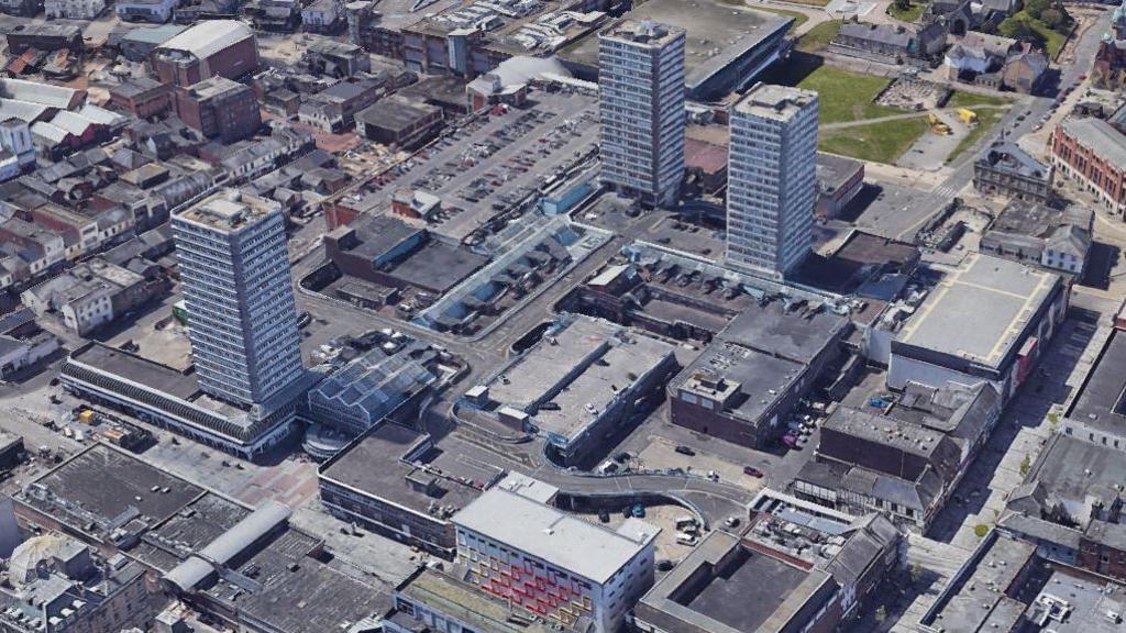 Aerial view of Sunderland City Centre. There are three tall tower blocks surrounding a shopping centre and various other buildings and plazas around.