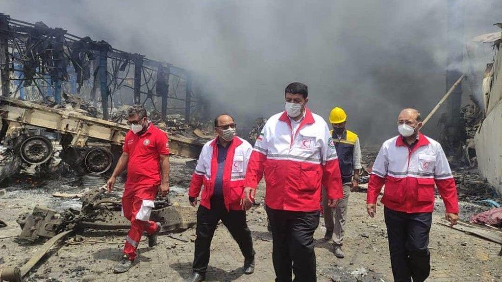Rescue workers walk among the smoke and charred rubble at site of port blast.