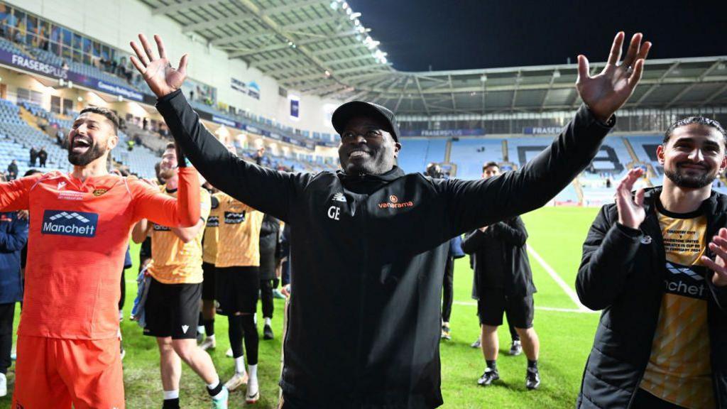 George Elokobi and Maidstone's players embrace fans with their arms aloft after their defeat by Coventry