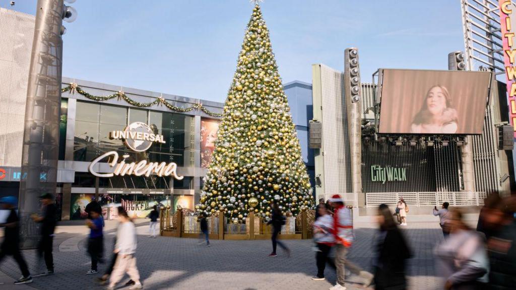 A shot of a CityWalk area outside a Universal Park in america. A building called "Universal Cinema" can be seen, it has a big Christmas tree outside.