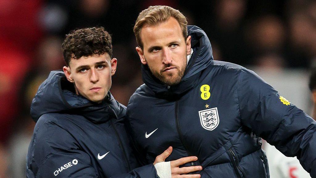 Phil Foden and Harry Kane after the final whistle at Wembley, with both wearing blue England team coats and Foden with his right hand across Kane's chest