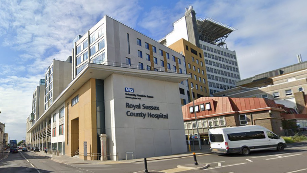 A generic external shot of the hospital with its name in large letters on the side of a grey wall. 