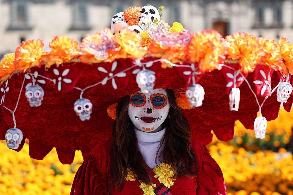 A lady is dressed as La Catrina, an iconic skeleton feature associated with Dia De Los Muertos, wearing a hat with mini skulls.