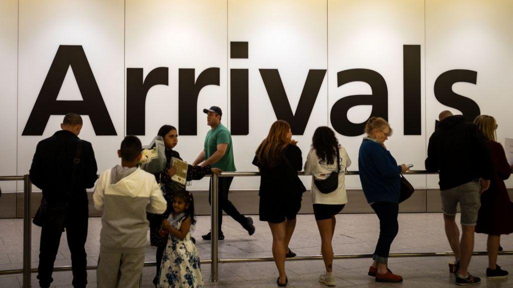 People wait to greet friends and relatives in front of a huge sign reading "Arrivals" at Heathrow Airport, Terminal 4, London.