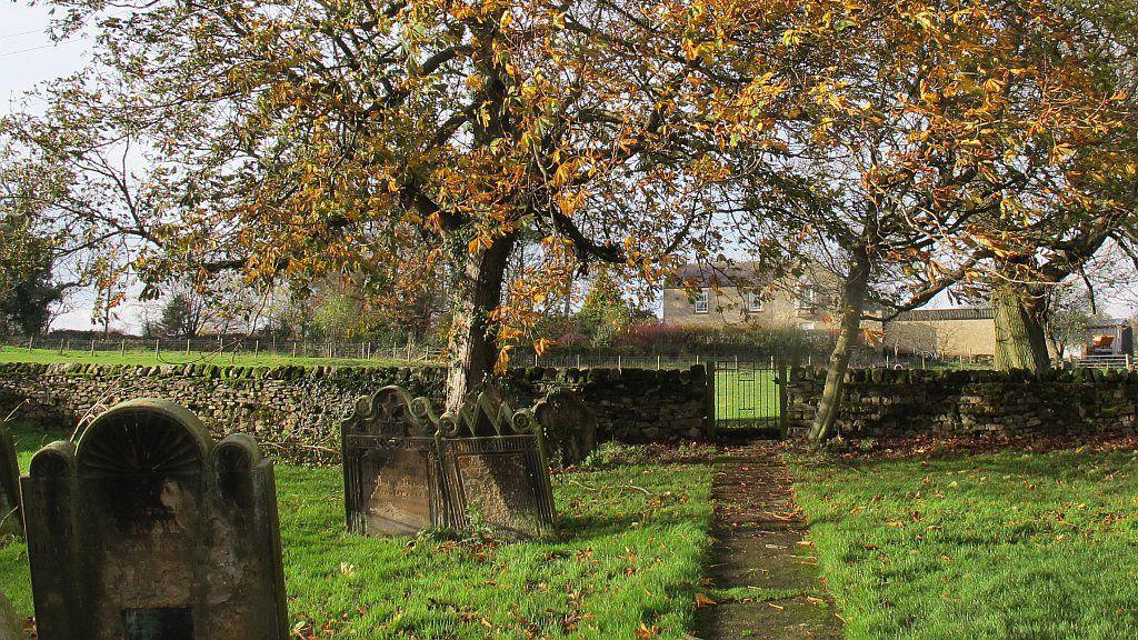 A small church graveyard with green grass and autumn trees