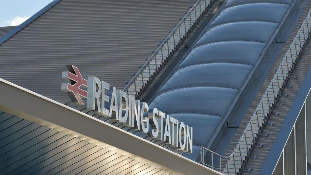 A close up of lettering on top of a silver building roof saying "Reading Station",